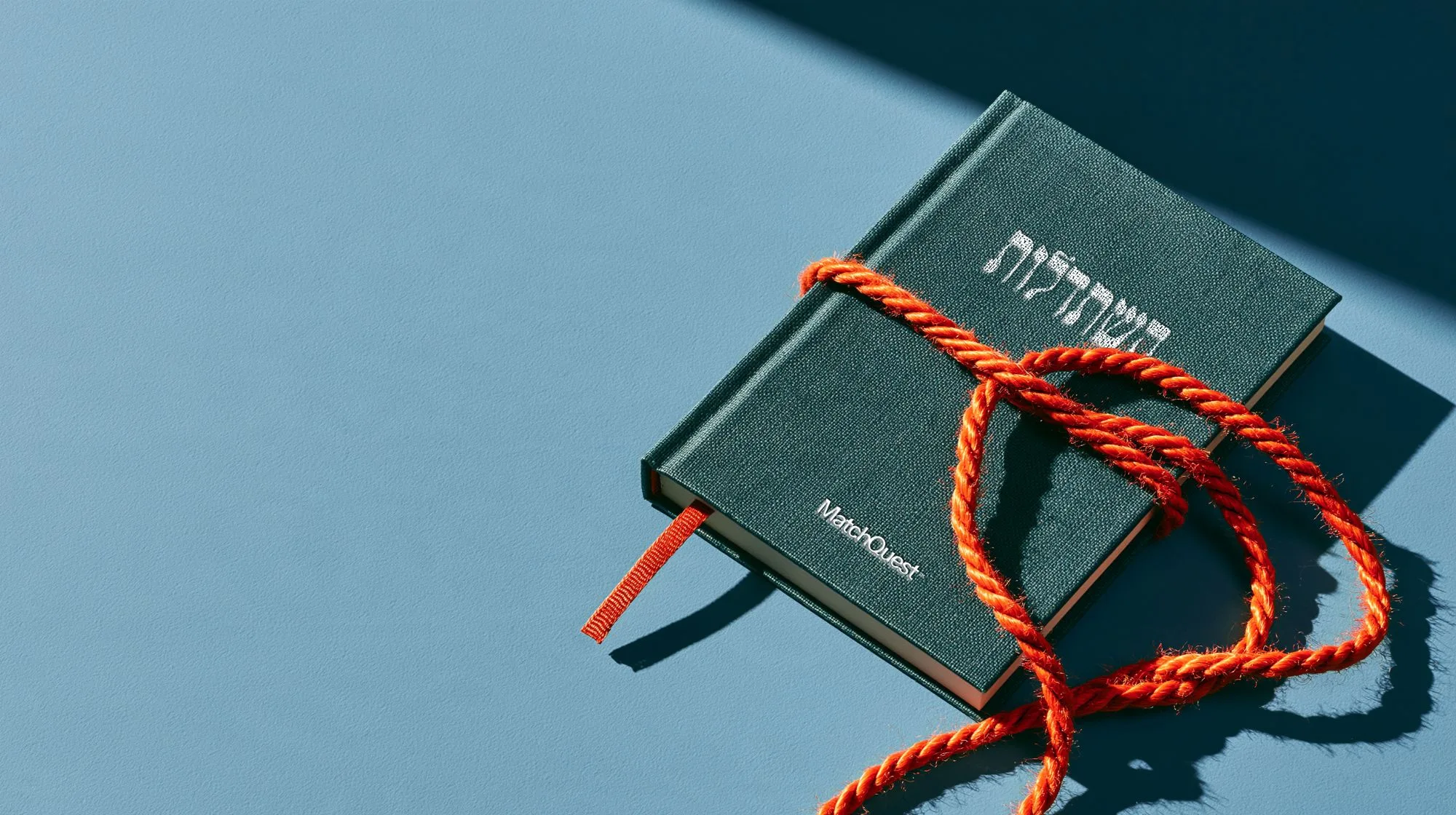 A green MatchQuest notebook wrapped in orange cord on a sky-blue table.